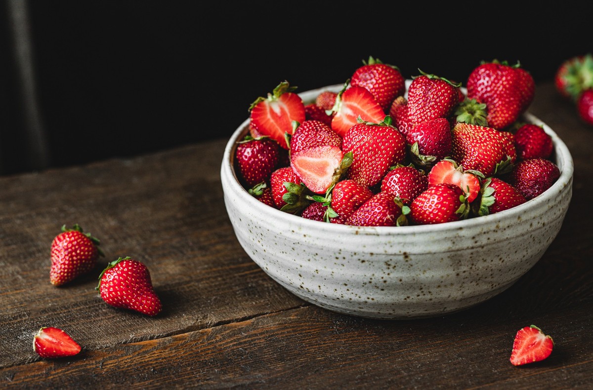 Close-up of bowl of fresh strawberries. Freshly harvested strawberries in a ceramic bowl over wooden table.