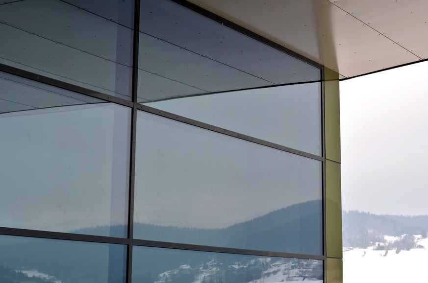 large glass shop windows with an overhang of the roof are a mirror of the foothill landscape. metallic gold. wall and ceiling cladding sheets attached with rivets. halogen light in ceiling pattern