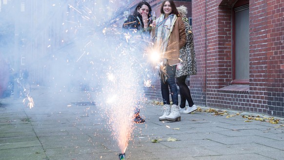 ILLUSTRATION - Drei junge Frauen stehen am 08.11.2017 vor einem Wohnhaus in Hamburg und schauen einem Bodenfeuerwerk zu (gestellte Szene). Foto: Christin Klose || Modellfreigabe vorhanden