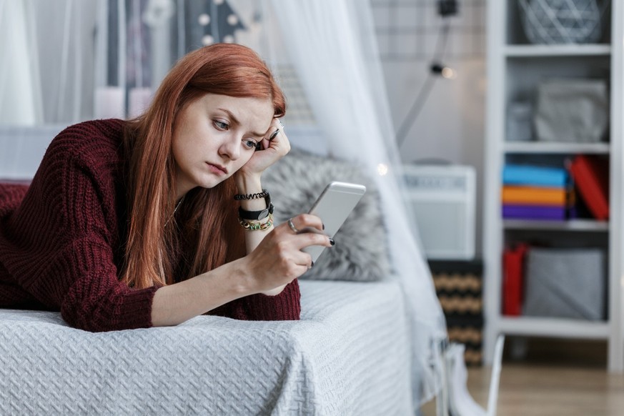 Worried, young teenager looking at the phone in her room