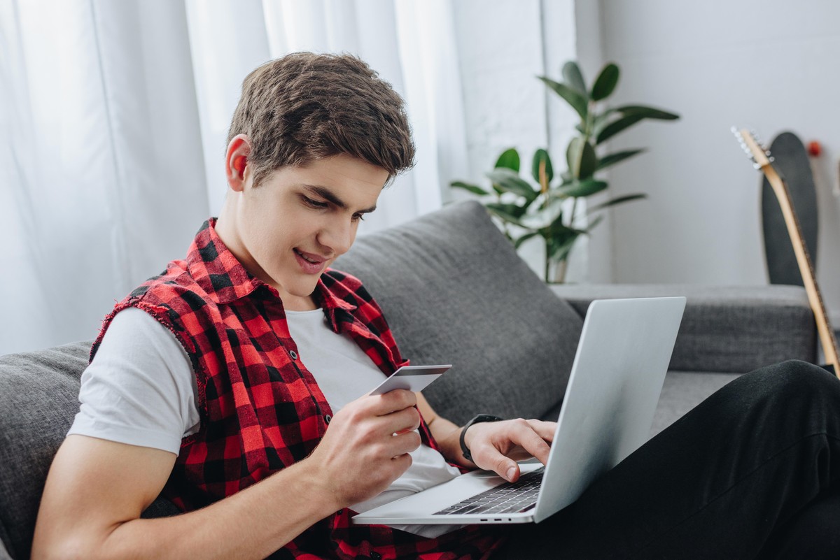 male teenager using laptop and paying with credit card at home