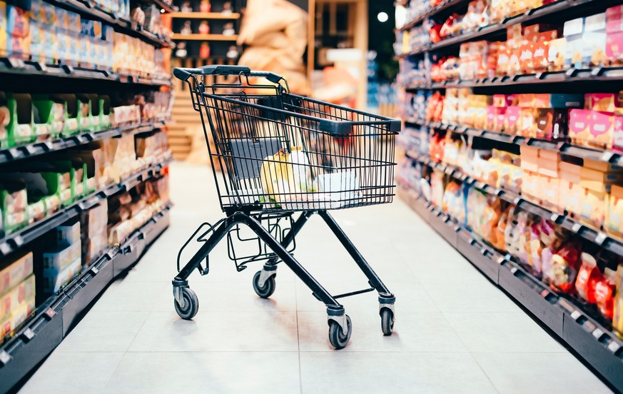 Abandoned shopping cart with groceries in the middle of the aisle in the supermarket. No one is on the photo.