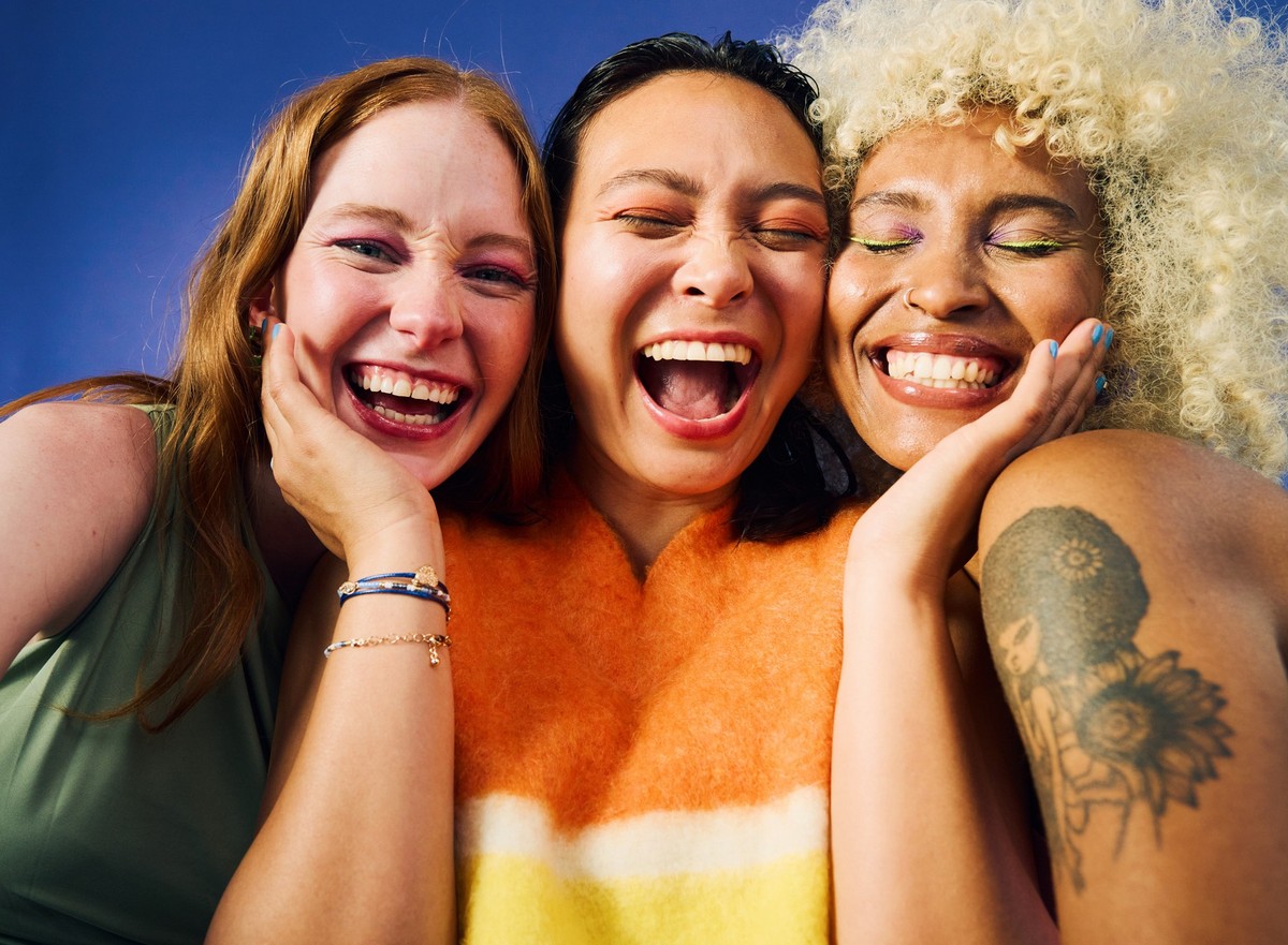 Three Gen Z women laughing together on blue background