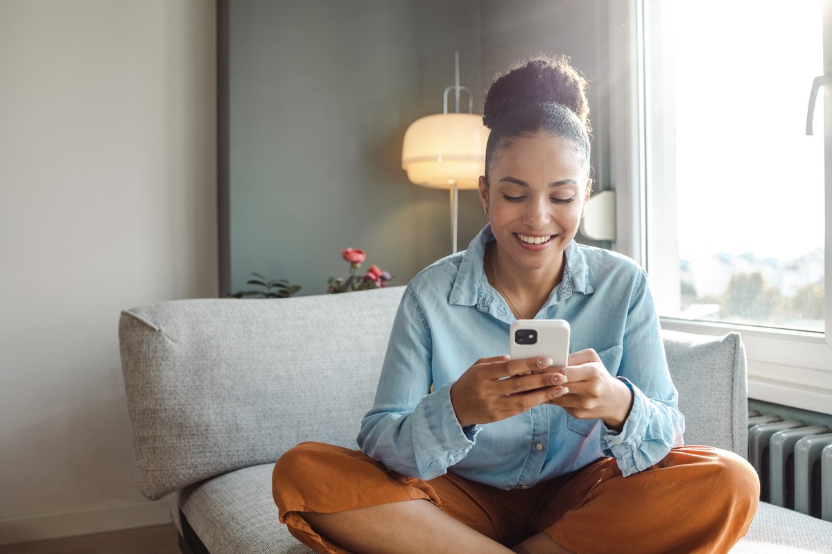 A young woman is at home in the living room, she is using a mobile phone and smiling