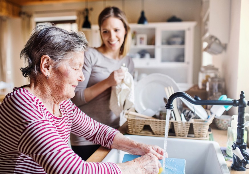 A happy elderly grandmother with an adult granddaughter at home, washing the dishes.