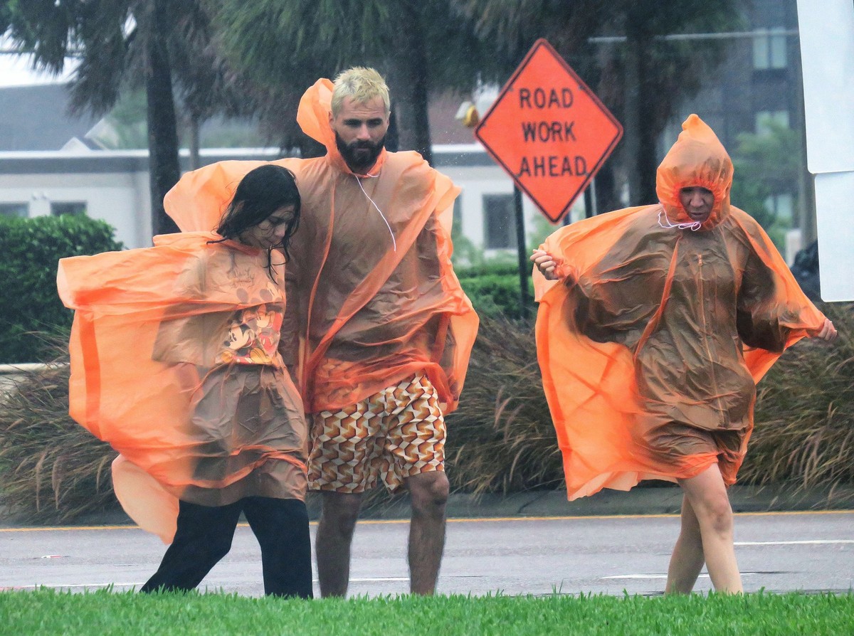 28.09.2022, USA, Orlando: Menschen tragen Regenumh�nge, w�hrend sie bei starken Windb�en, verursacht durch Hurrikans Ian, den International Drive in Orlando entlanggehen. Foto: Joe Burbank/Orlando Sen ...