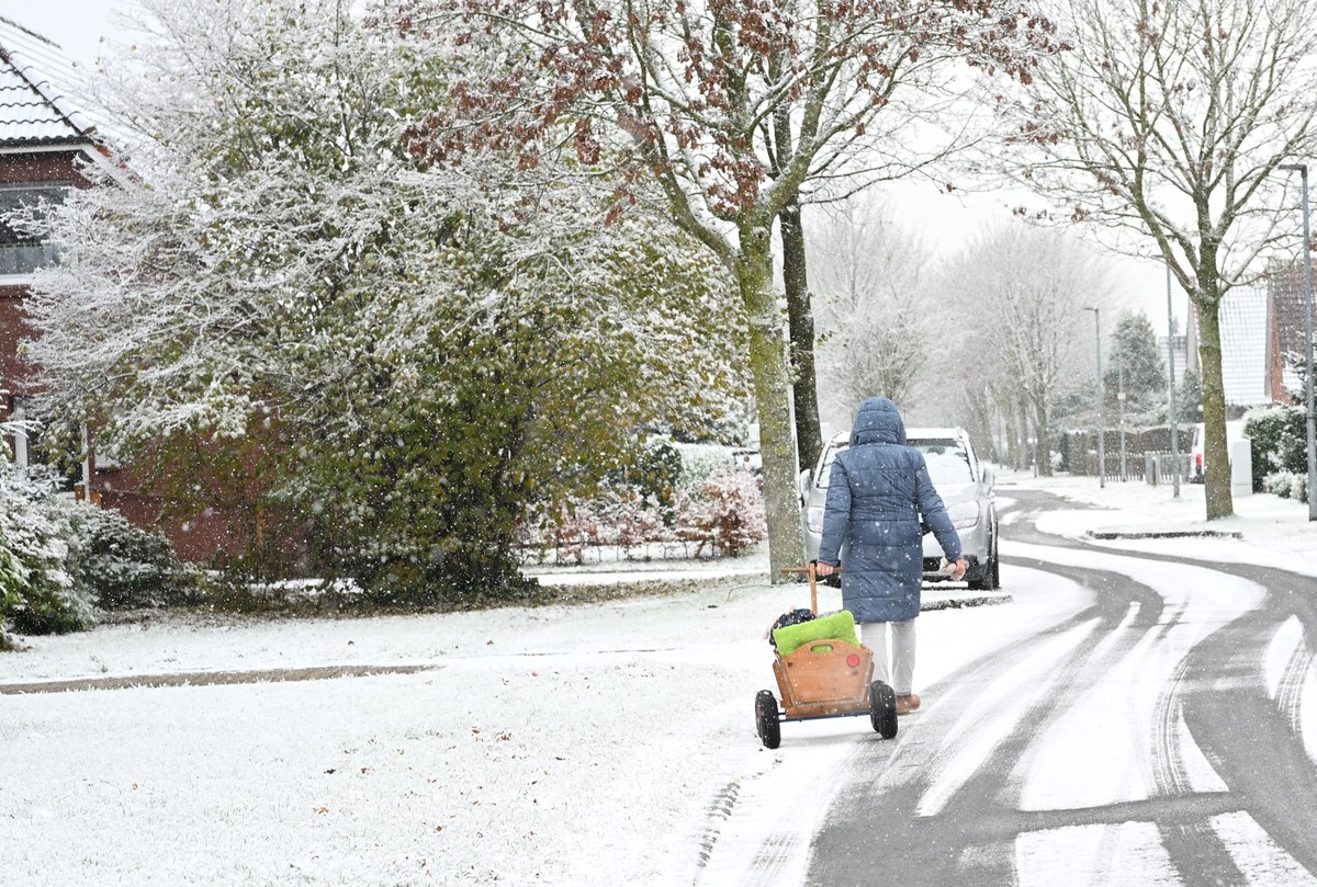 21.11.2025, Niedersachsen, Warsingsfehn: Eine Frau zieht mit einem Bollerwagen über eine mit Schnee bedeckte Straße. Auch im Nordwesten Deutschlands herrscht winterliches Wetter. Foto: Lars Penning/dp ...
