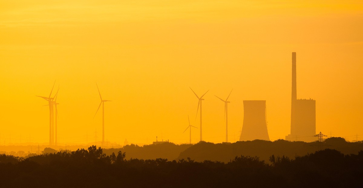 [M] Ein gelbes, zerkratztes Hinweisschild mit der Aufschrift &quot;Energiewende&quot; vor einigen Windkraftanlagen und einem im Aufbau befindlichen Freileitungsmast. Composing als Symbolbild in Bezug  ...