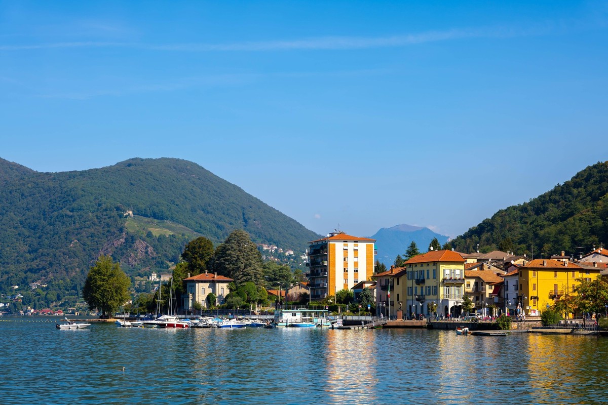 Stadt Porto Ceresio am Wasser mit Berg und Luganer See an einem sonnigen Sommertag in Porto Ceresio, Lombardei, Italien, Europa *** City Porto Ceresio on Water with mountain and Lugano Lake to a sunny ...