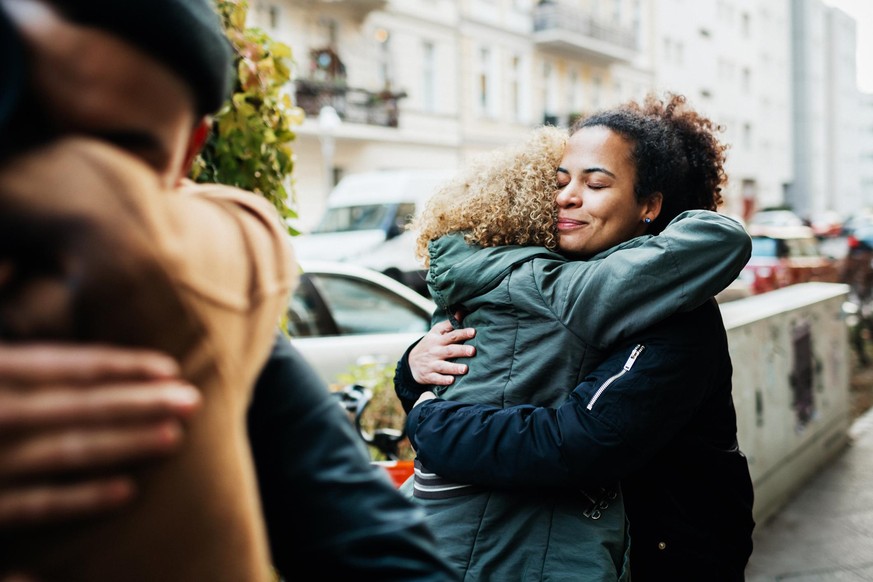 A couple of friends embracing in the street while they meet up to go for a drink.