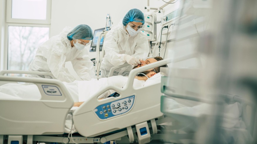 Coronavirus covid-19 infected patient in a quarantine ward at the hospital with doctors in protective suits while they making disease treatment of him