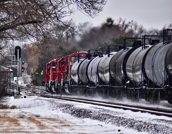 A crude oil train passes by in the winter, creating snow drift at the wheels