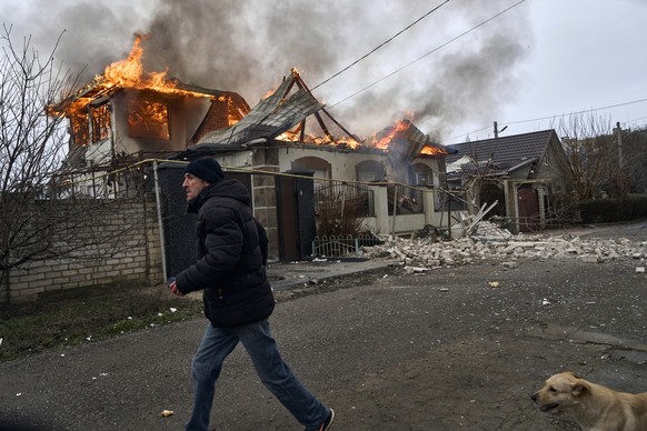 dpatopbilder - 06.01.2023, Ukraine, Cherson: Ein Anwohner läuft an einem brennenden Haus vorbei, das nach ukrainischen Angaben bei russischem Beschuss am orthodoxen Weihnachtsabend getroffen wurde. Fo ...