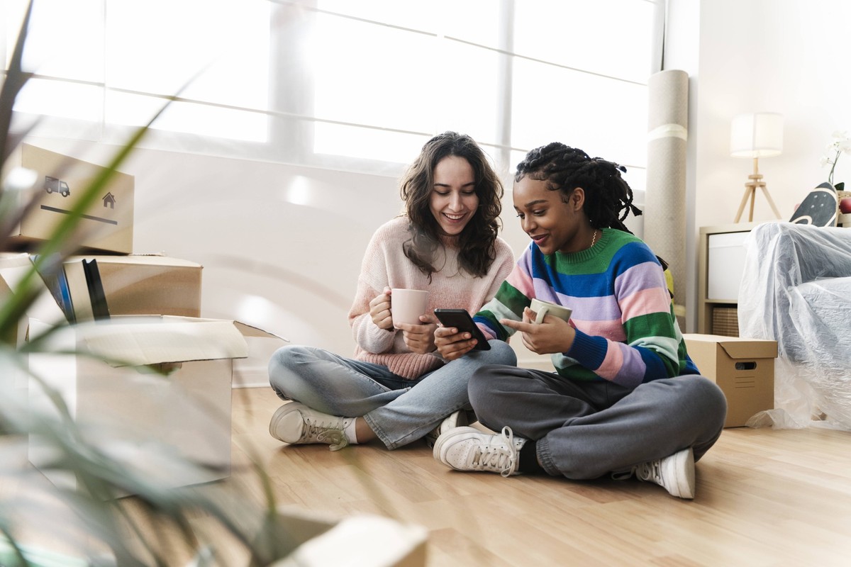 Happy young woman sharing mobile phone with friend at home model released, Symbolfoto property released, JCZF01180