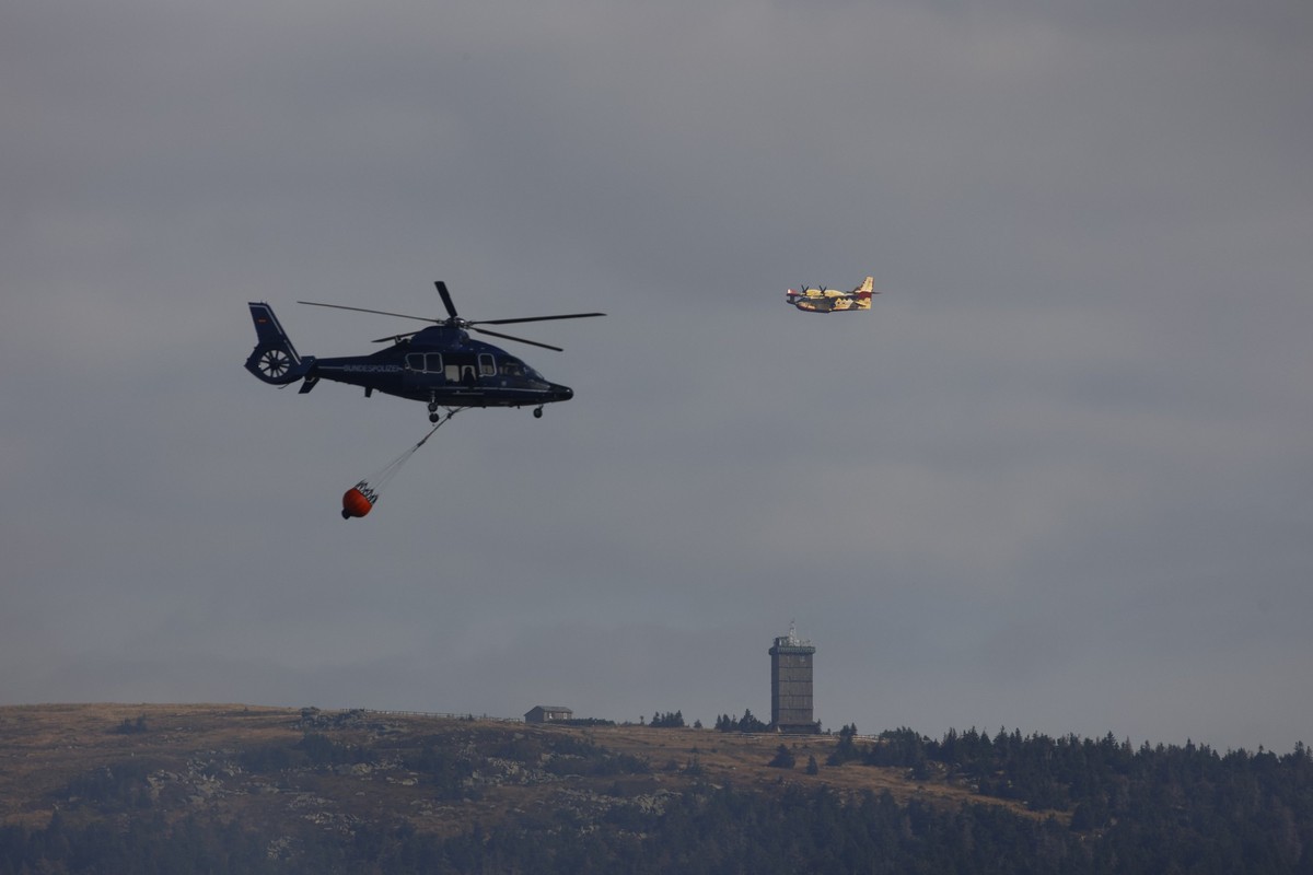 05.09.2022, Sachsen-Anhalt, Schierke: Ein Löschhubschrauber der Bundespolizei bekämpft den Waldbrand aus der Luft, im Hintergrund fliegt ein Löschflugzeug der italienischen Feuerwehr. Am Brocken brenn ...