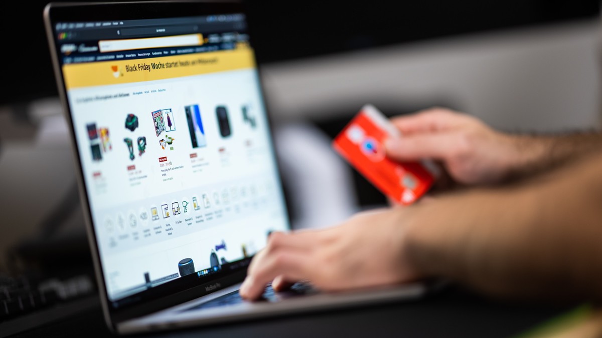 ARCHIV - 18.11.2021, Niedersachsen, Oldenburg: Ein Mann mit einer Bankkarte in der Hand sitzt am Laptop und schaut sich die Black Friday Angebote auf der Online-Shopping-Seite von Amazon an. Bei Männe ...