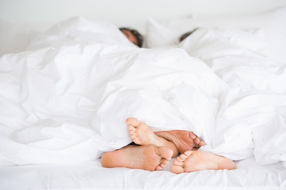Male and female feet in bed under blankets