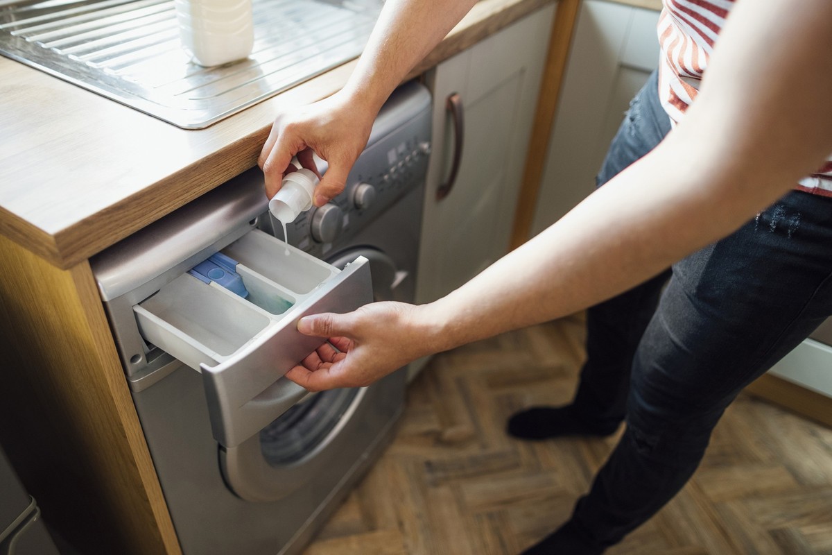 High angle view of a man pouring laundry detergent into a washing machine in his kitchen. He is in the Northeast of England.