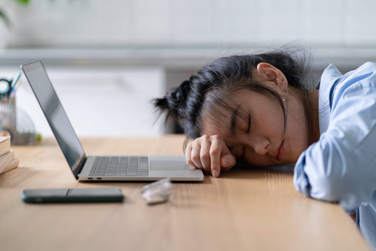 Müdes asiatisches Studentenmädchen, das auf dem Tisch vor dem Laptop schläft und eine Pause beim Online-Lernen macht Müdes asiatisches Studentenmädchen, das auf dem Tisch vor dem Laptop schläft und ei ...