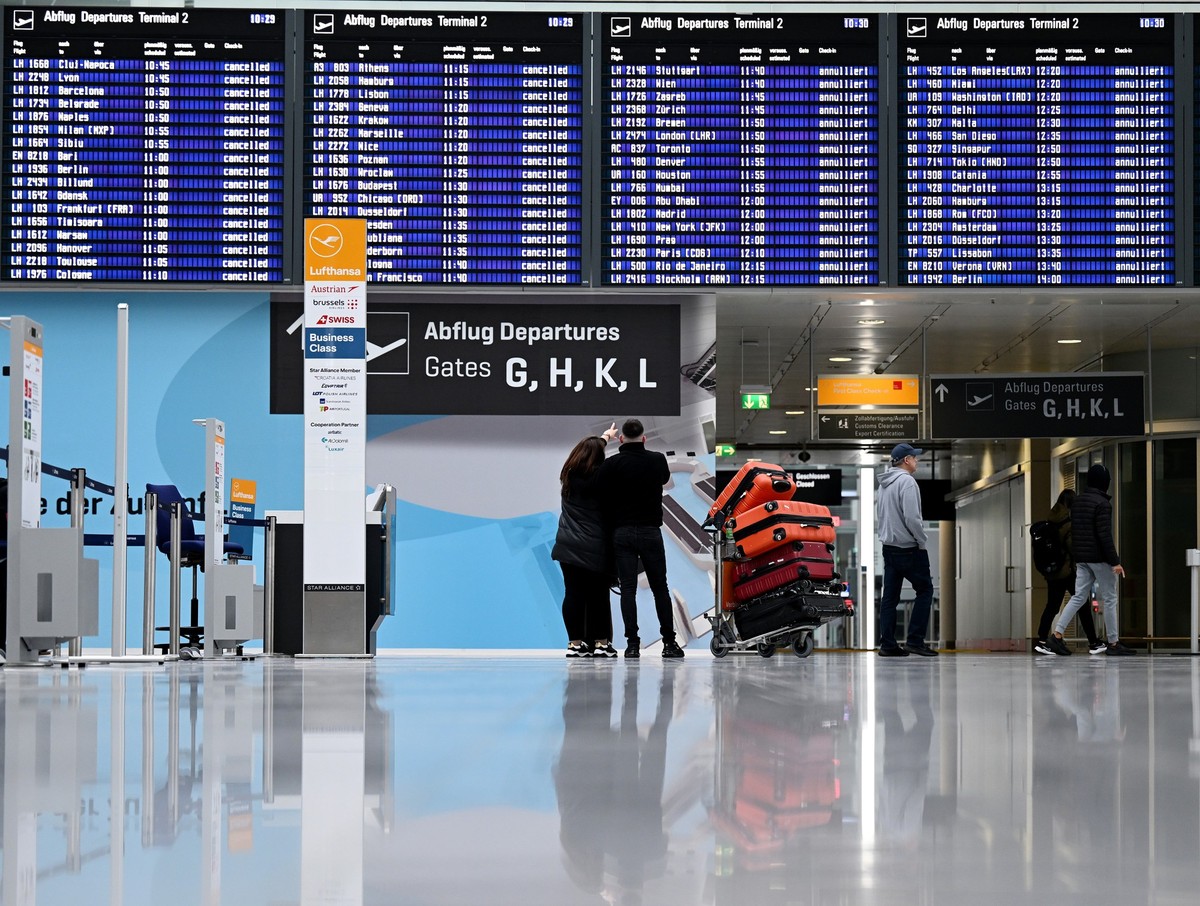 ARCHIV - 26.03.2023, Bayern, München: Passagiere stehen im Münchner Flughafen vor der Anzeigentafel. Wegen eines angekündigten Eisregens wird es am Münchner Flughafen am Dienstag von Betriebsbeginn bi ...