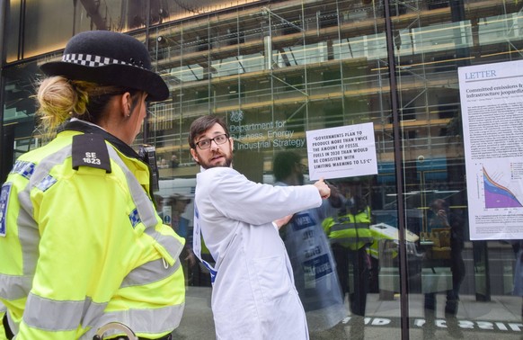 April 13, 2022, London, England, United Kingdom: A scientist with his hand superglued to the window explains why they are protesting to a police officer. Scientists glued themselves to the Department  ...