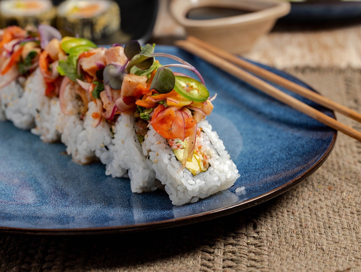 Close-up of sushi rolls topped with fresh vegetables and fish on a blue plate with chopsticks, showcasing vibrant colors and textures. 29570550 RECORD DATE NOT STATED