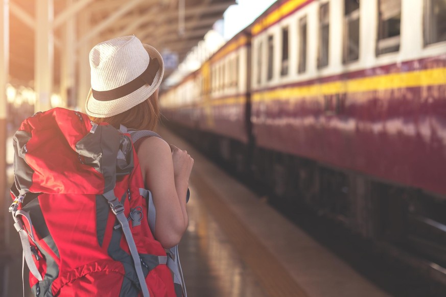 Traveler with backpack waiting for a train at train station. Travel and vacation concept.