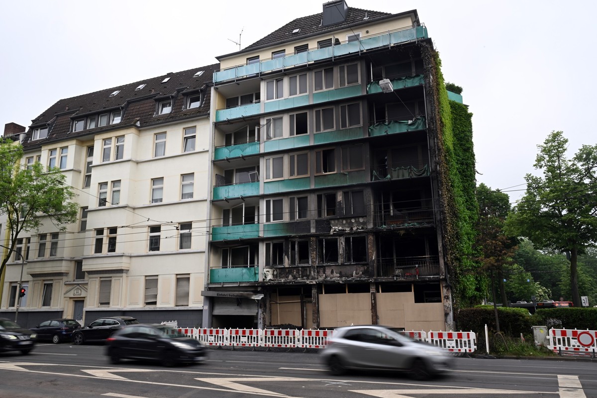 17.05.2024, Nordrhein-Westfalen, Düsseldorf: Autos fahren an dem Haus vorbei, in dem ein Feuer wütete. Nach der Explosion und dem verheerenden Feuer in einem Wohn- und Geschäftshaus in Düsseldorf mit  ...