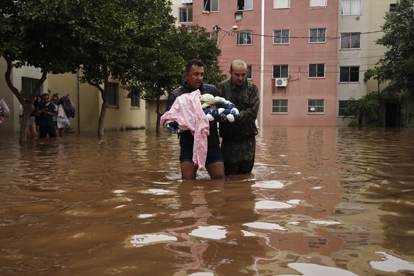 dpatopbilder - 04.05.2024, Brasilien, Canoas: Ein Mann, der ein Baby trägt, watet durch eine überschwemmte Straße. Bei Überschwemmungen nach tagelangem Regen ist die Zahl der Toten im Süden Brasiliens ...