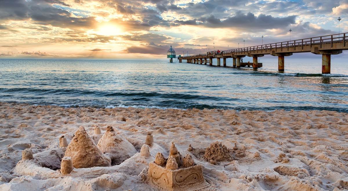 Pier and beach with sand castles in foreground in Zinnowitz at sunset. Baltic Sea, island Usedom, Germany
