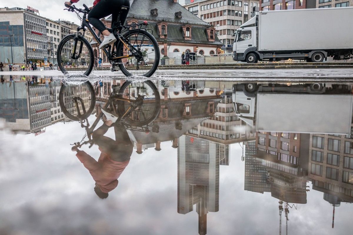 10.03.2023, Hessen, Frankfurt/Main: Eine Radfahrerin und Hochhäuser spiegeln sich in einer großen Pfütze, die sich bei Regenwetter an der Hauptwache in der Innenstadt gebildet hat. Foto: Frank Rumpenh ...