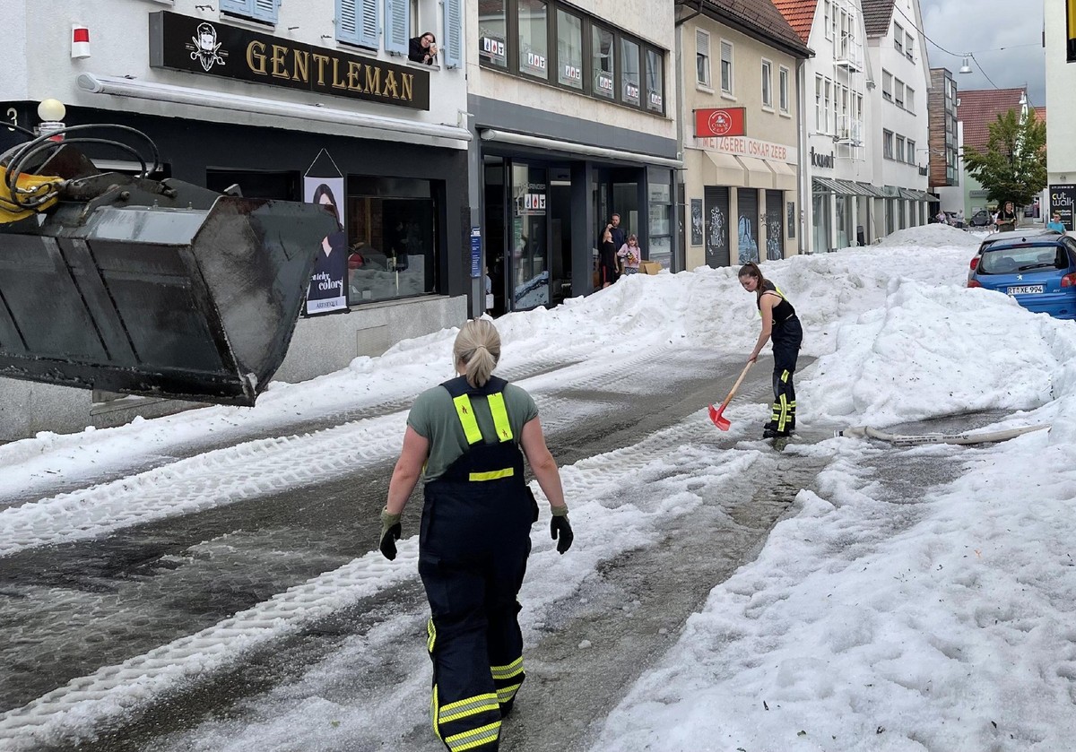 ARCHIV - 04.08.2023, Baden-Württemberg, Reutlingen: Einsatzkräfte der Feuerwehr räumen Hagel von einer Straße. Winterdienst-Einsatz mitten im Sommer: Ein lokal begrenztes Unwetter hat Straßen in der I ...