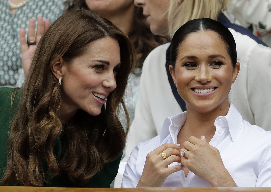 FILE - In this Saturday, July 13, 2019, file photo, Kate, Duchess of Cambridge, left, and Meghan, Duchess of Sussex chat as they sit in the Royal Box on Centre Court to watch the women's singles final ...