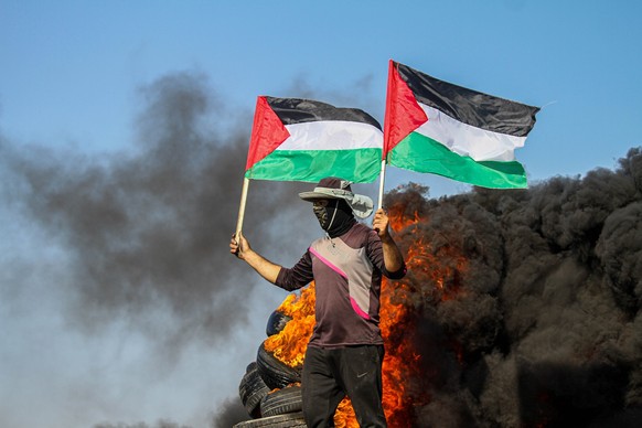 03.07.2023, Palästinensische Gebiete, Malika: Palästinenser verbrennen Reifen und schwenken die palästinensische Nationalflagge während einer Demonstration in der Gegend von Malika im östlichen Gazast ...