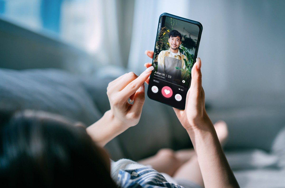 Young Asian woman lying on sofa at home, using an online dating app on smartphone, looking for love on the internet. Social media. Internet dating. Couple relationship. Love concept