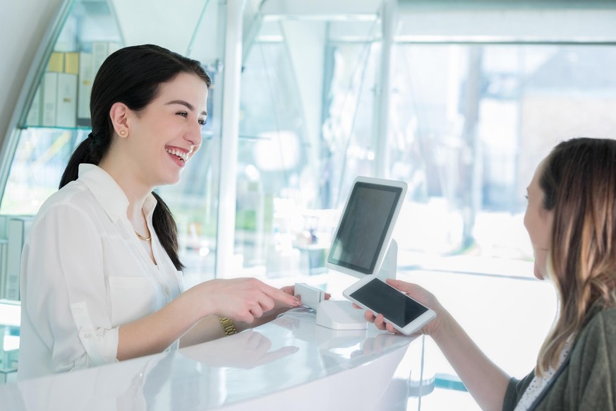 Mid adult female hair salon customer uses contactless payment to pay for haircut and style.