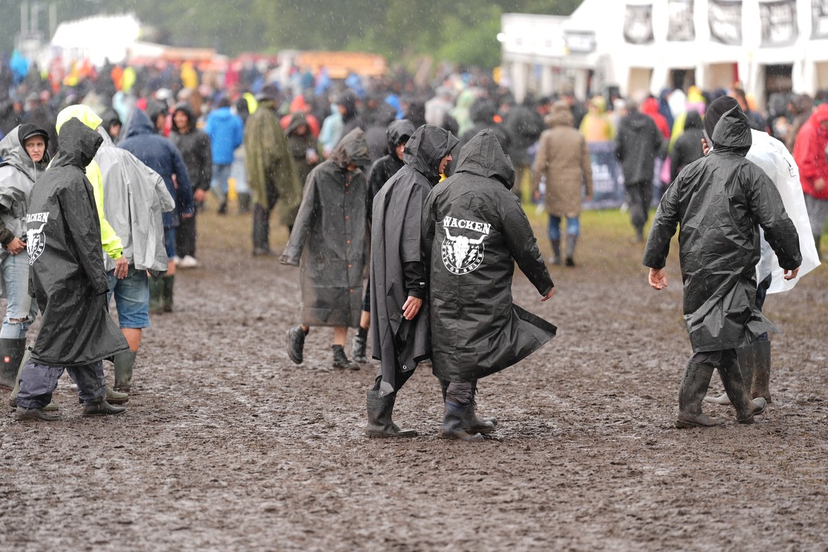 30.07.2025, Schleswig-Holstein, Wacken: Metal-Fans gehen durch den Matsch auf dem Festivalgelände des Wacken Open Airs. Das Wacken Open Air (WOA) findet vom 30. Juli bis 2. August statt und gilt als g ...