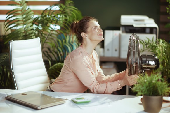 Sustainable workplace. happy modern female employee in modern green office with electric fan.
