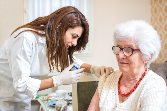 Home healthcare nurse giving injection to elderly woman.