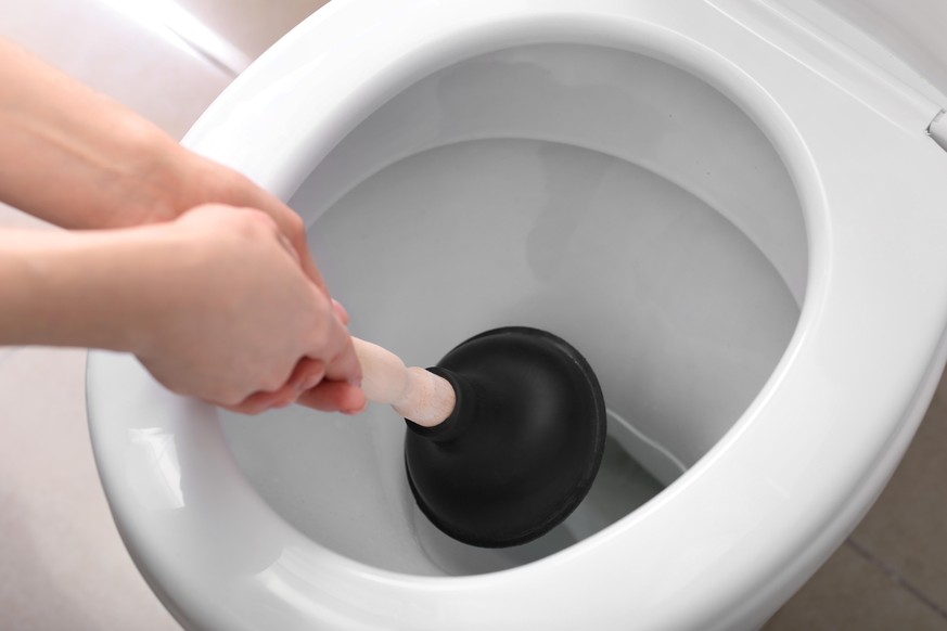 Young woman using plunger to unclog a toilet bowl