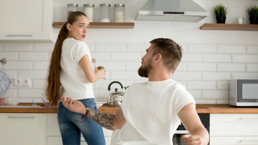 Angry husband and shocked insulted wife arguing in the kitchen, hungry mad boyfriend scolding offended girlfriend for bad cooking, unhappy couple having conflict quarrel disagree about food at home