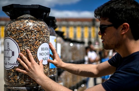 A man reads a sticker reading &quot;Cigarette butts on the ground, no!&quot; on a container full of butts collected in a week, at Comercio square in Lisbon on April 23, 2023. - Environmental activists ...