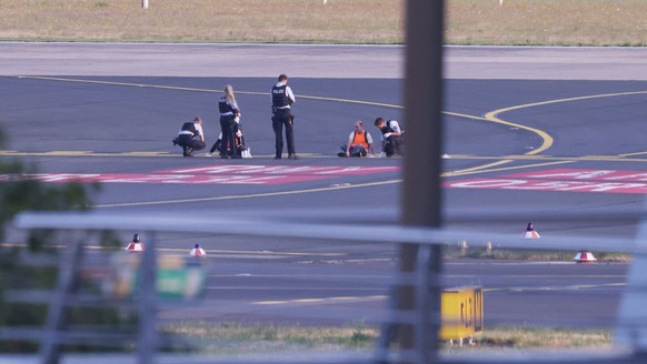 13.07.2023, Nordrhein-Westfalen, Düsseldorf: Polizisten stehen auf dem Flugfeld und versuchen Aktivisten der Gruppe Letzte Generation am Flughafen vom Asphalt zu lösen, nachdem sie sich festgeklebt ha ...