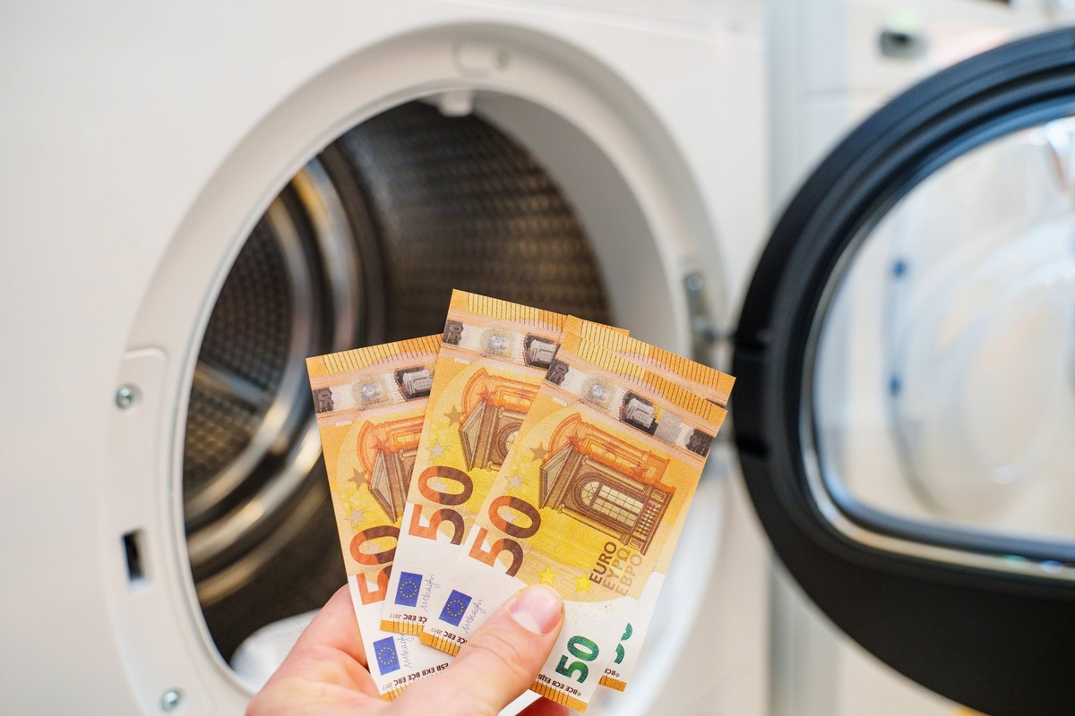 Augsburg, Bavaria, Germany - September 2, 2023: Hand holding 50 euro banknotes in front of a washing machine *** Hand hält 50 Euro Geldscheine vor eine Waschmaschine