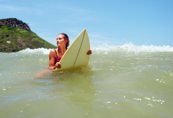 portrait mid adult caucasian woman holding on surfboard on the crest of the wave.