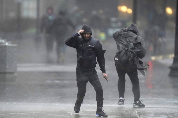 18.12.2023, USA, Boston: Menschen überqueren bei Wind und starken Regen eine Straße. Bei einem heftigen Unwetter sind an der Ostküste der USA Medienberichten zufolge mehrere Menschen ums Leben gekomme ...