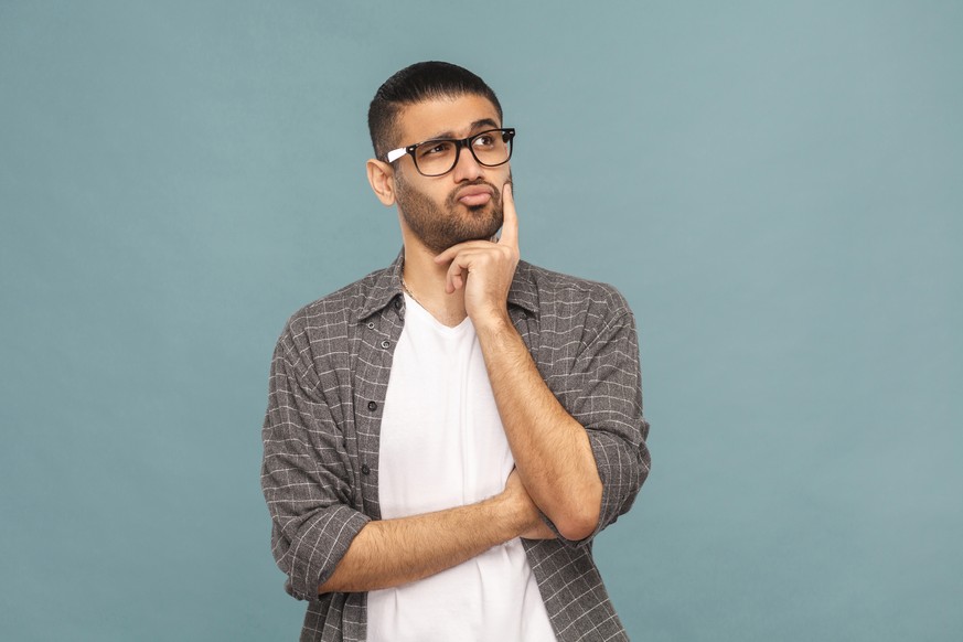 Portrait of bearded thoughtful handsome man with black glasses in casual style thinking. studio shot on blue background.