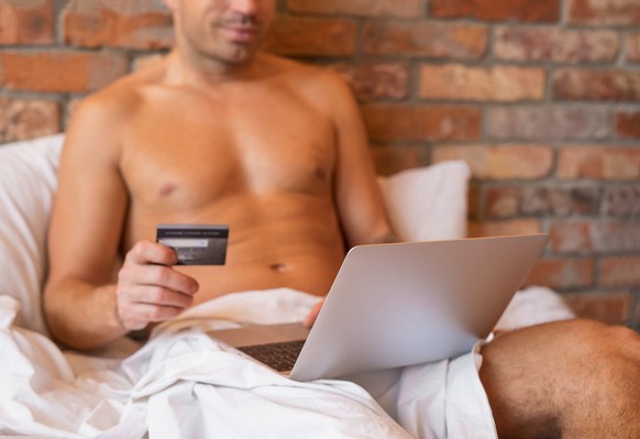 Man sitting in bed and paying with credit card for something using laptop