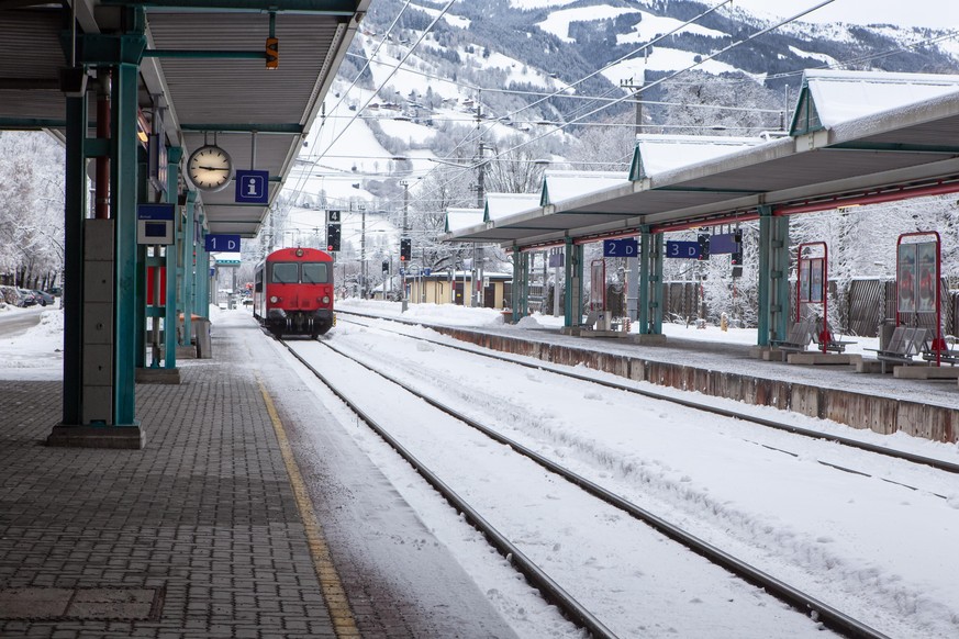 Red passenger high-speed train pulls up to stop at deserted snow-covered railway station in mountains. Concept of transport, communication, infrastructure, travel in Europe. Horizontal format.