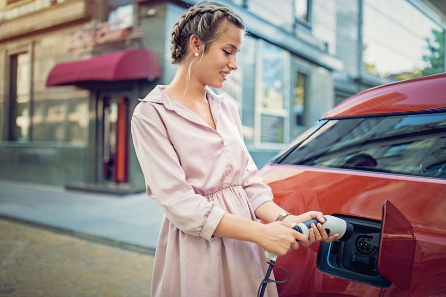 Young girl is charging her electric car in the city